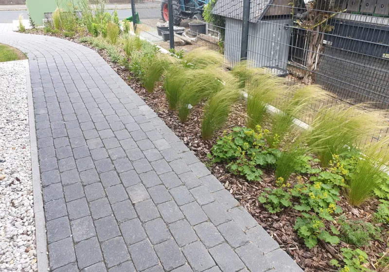 Gepflasterter Weg mit neu angelegten Beeten